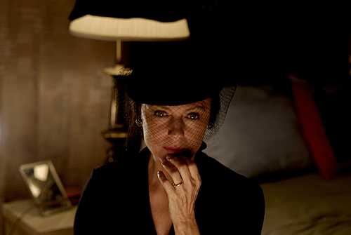 A woman wearing all black and a black hat and veil looking pensively toward the camera.