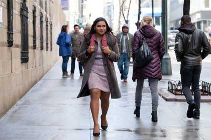 A woman walking along a busy city sidewalk looking optimistic.